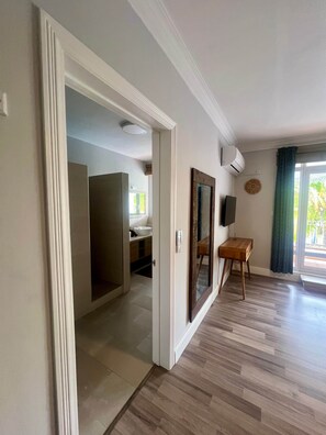 Una habitación con suelo de madera, un escritorio de madera, un televisor y una ventana con cortinas.