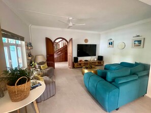 A living room with a teal sofa, a flat-screen TV, a staircase, and a ceiling fan.