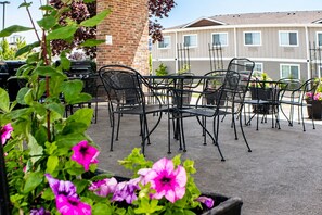 An outdoor patio with metal chairs and tables, surrounded by potted plants and a brick wall. - Kitchen King Suite in Moses Lake | Free Breakfast (Moses Lake)