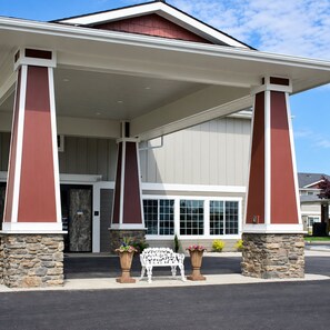 A building with a covered entrance, stone pillars, and a bench with potted plants. - Kitchen King Suite in Moses Lake | Free Breakfast (Moses Lake)
