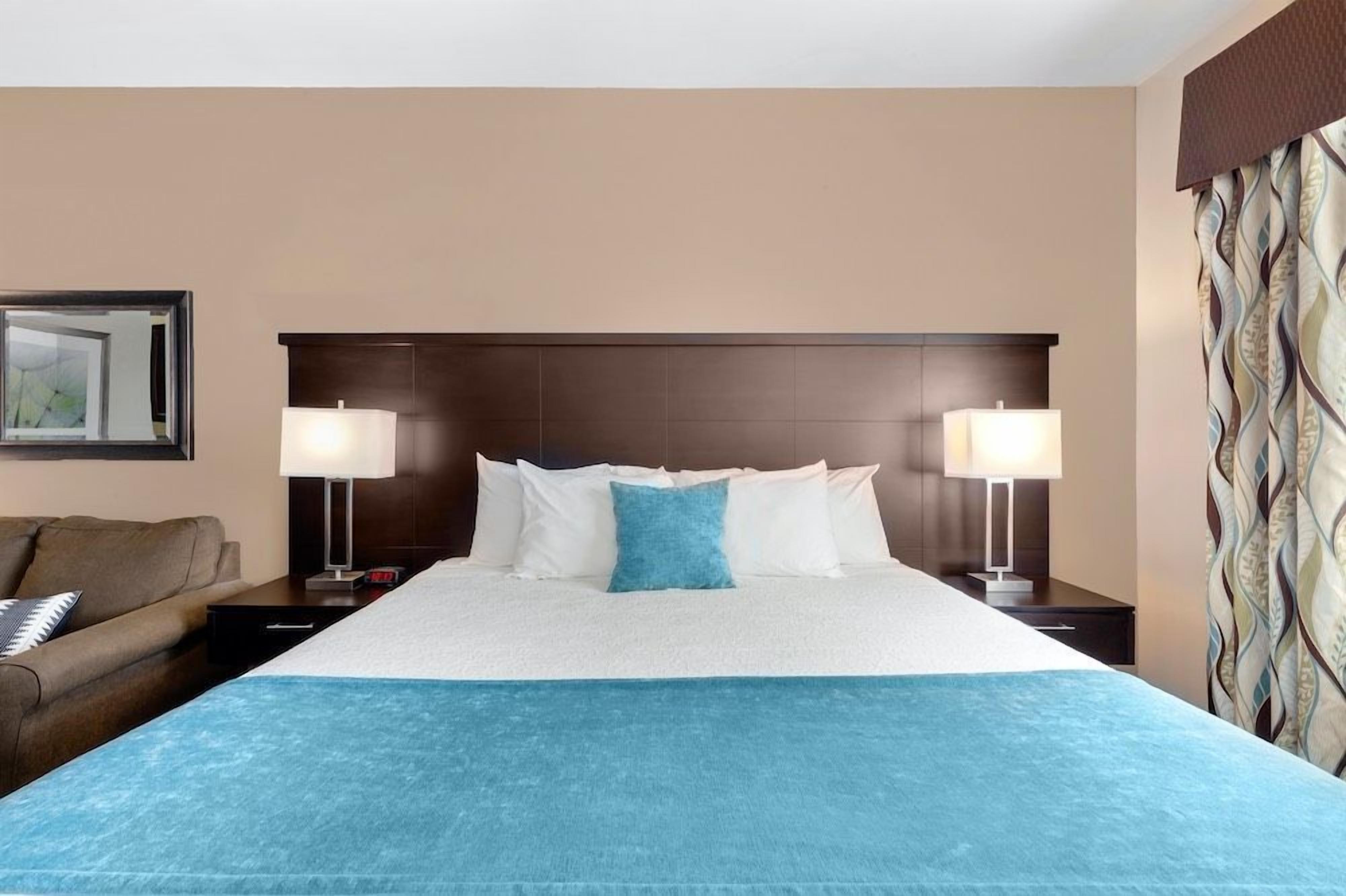 A hotel room with a large bed, two bedside lamps, a nightstand, a sofa, and a patterned curtain.