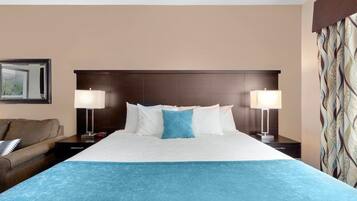 A hotel room with a large bed, two bedside lamps, a nightstand, a sofa, and a patterned curtain.