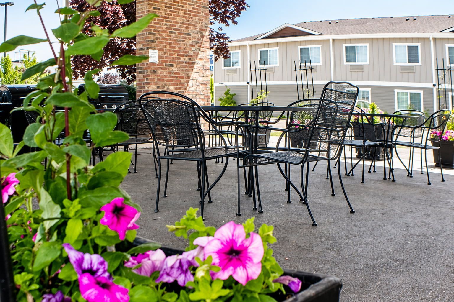 An outdoor patio with metal chairs and tables, surrounded by potted plants and a brick wall.