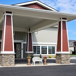 A building with a covered entrance, stone pillars, and a bench with potted plants.