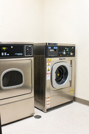 Two commercial-grade front-loading washing machines in a corner. - ADA Queen Room w/ Kitchen & Free Breakfast (Moses Lake)
