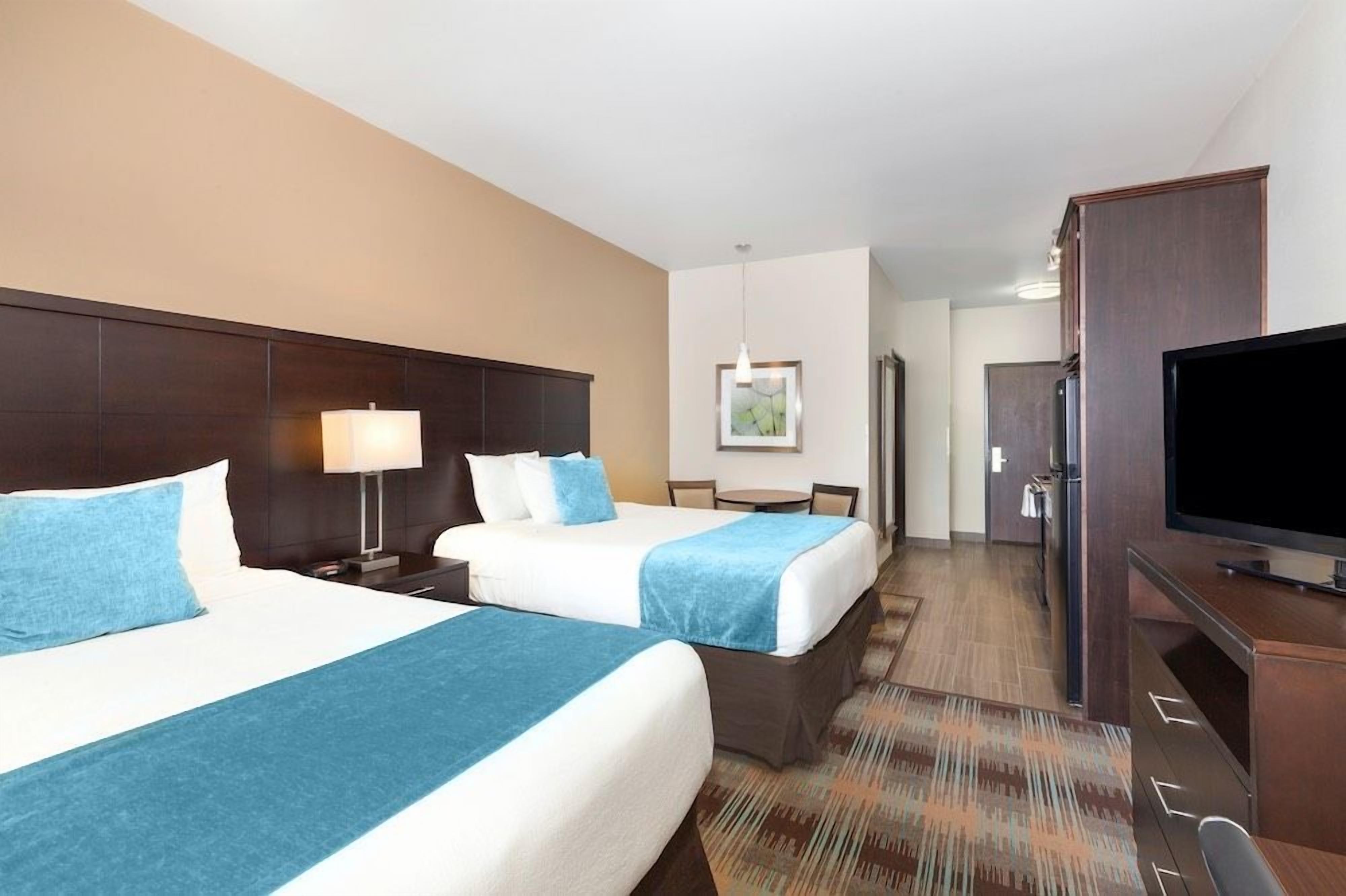A hotel room with two beds, a desk, a television, and a dining area.