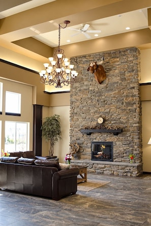 A spacious living room with a stone fireplace, a leather sofa, and a chandelier. - ADA Queen Room w/ Kitchen & Free Breakfast (Moses Lake)