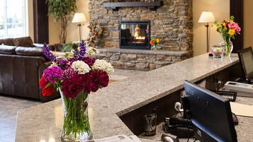 A hotel reception area with a stone fireplace, a vase of flowers, and a newspaper on the counter.