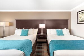 A hotel room with two beds, a nightstand, a lamp, and a framed picture on the wall.