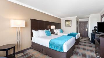 A hotel room with two beds, a desk, a television, and a floor lamp.