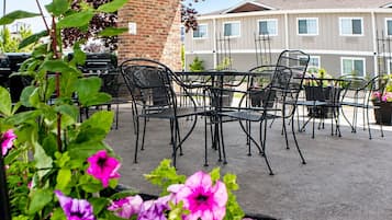 Een buitenpatio met metalen stoelen en tafels, omgeven door potplanten en een bakstenen muur.