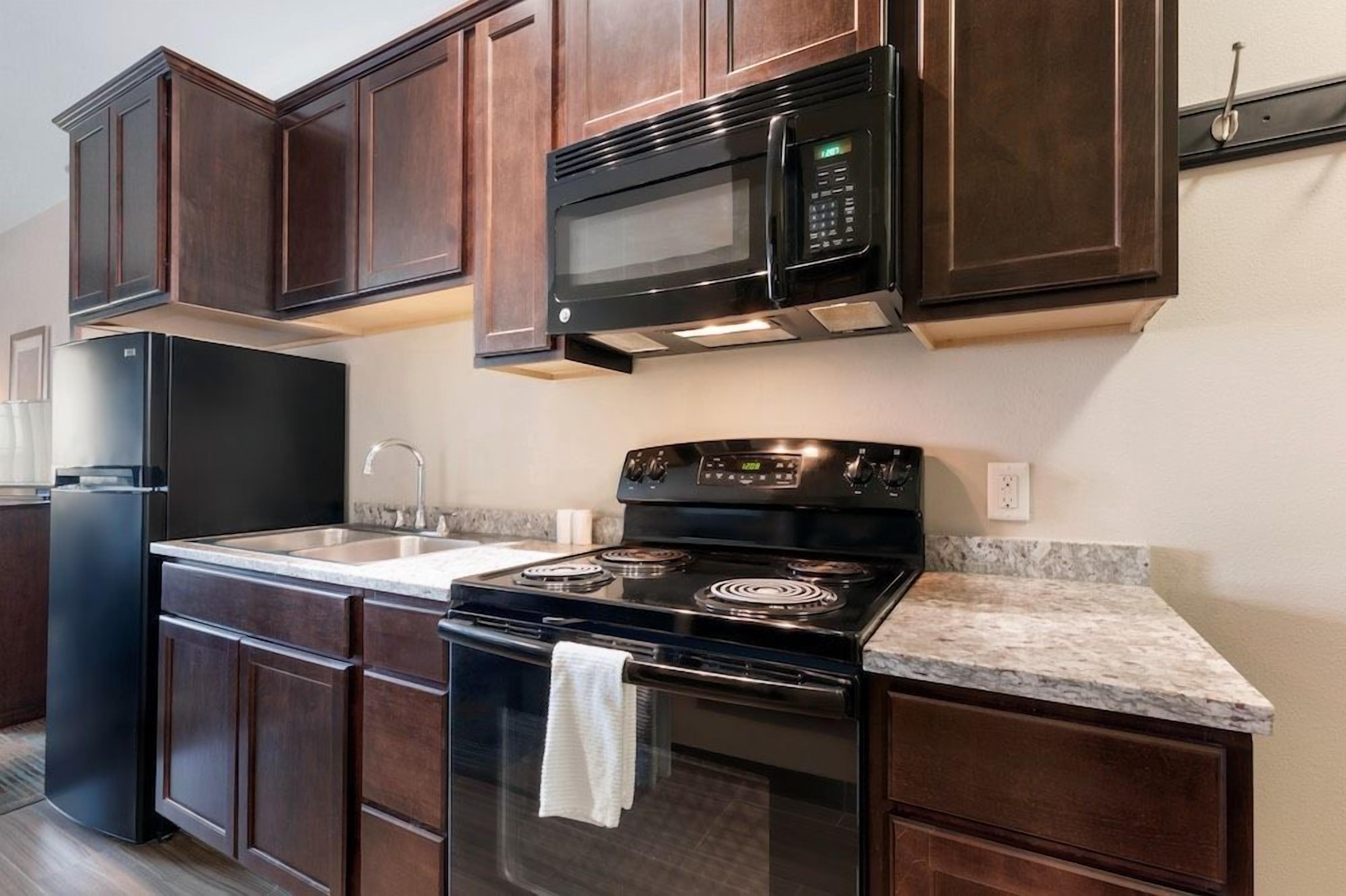 A kitchen with dark wood cabinets, a black microwave, a stove, and a refrigerator.