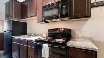 A kitchen with dark wood cabinets, a black microwave, a stove, and a refrigerator.