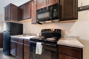 A kitchen with dark wood cabinets, a black microwave, a stove, and a refrigerator. - Suite w/ Full Kitchen + Breakfast | Nr Moses Lake (Moses Lake)