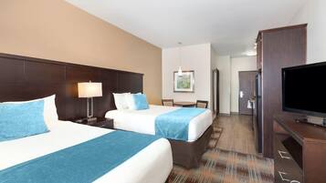 A hotel room with two beds, a desk, a television, and a dining area.