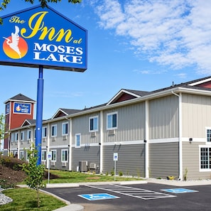 A hotel named 'The Inn at Moses Lake' with a signboard, a parking area with handicapped parking, and a building with multiple windows and a red tower.