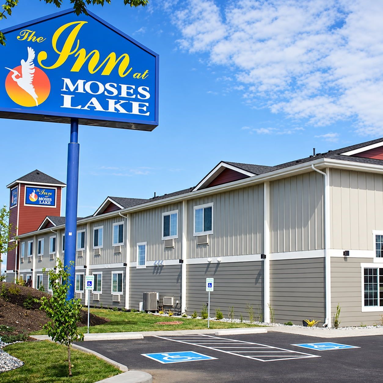 A hotel named 'The Inn at Moses Lake' with a signboard, a parking area with handicapped parking, and a building with multiple windows and a red tower.