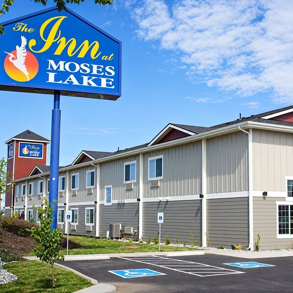 Et hotel kaldet 'The Inn at Moses Lake' med en skiltning, en parkeringsplads med handicapparkering og en bygning med mange vinduer samt et rødt tårn.