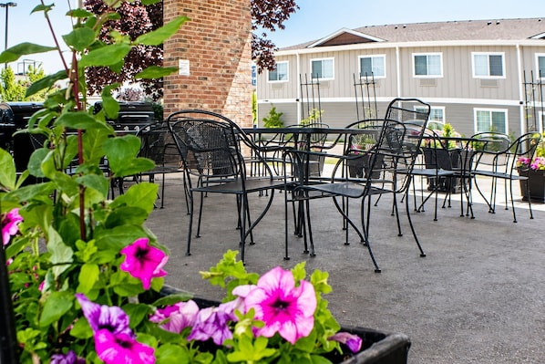 Une terrasse extérieure avec des chaises et des tables en métal, entourée de plantes en pot et d’un mur de briques.
