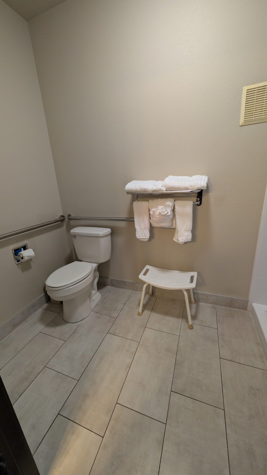 Un baño con inodoro, toallero y un pequeño banco.