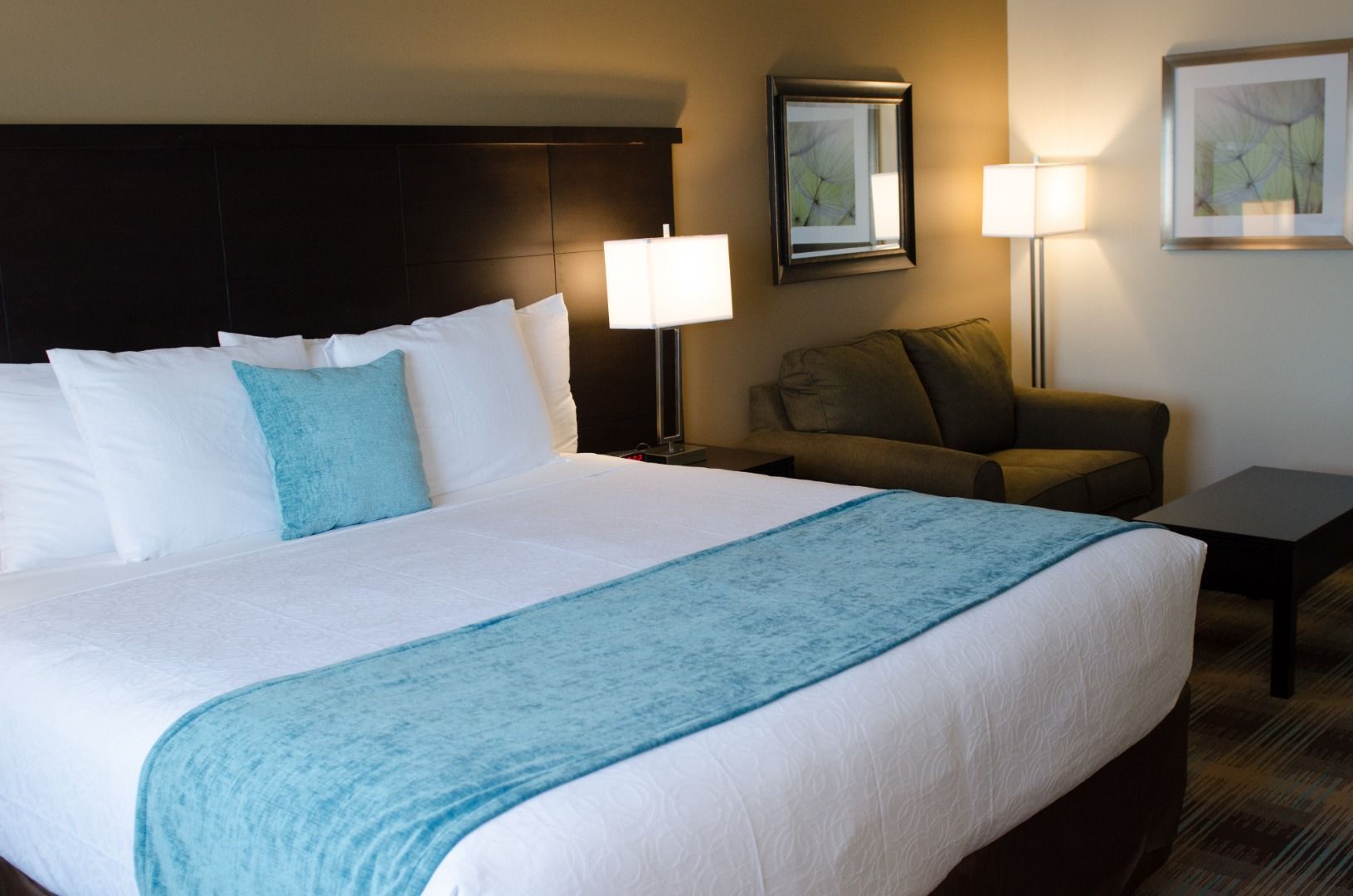 A hotel room with a large bed, two bedside lamps, a sofa, a small table, and a framed picture on the wall.