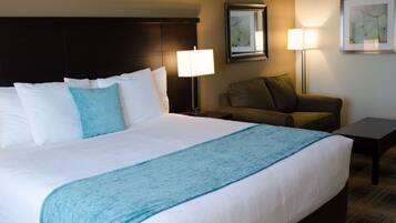 A hotel room with a large bed, two bedside lamps, a sofa, a small table, and a framed picture on the wall.