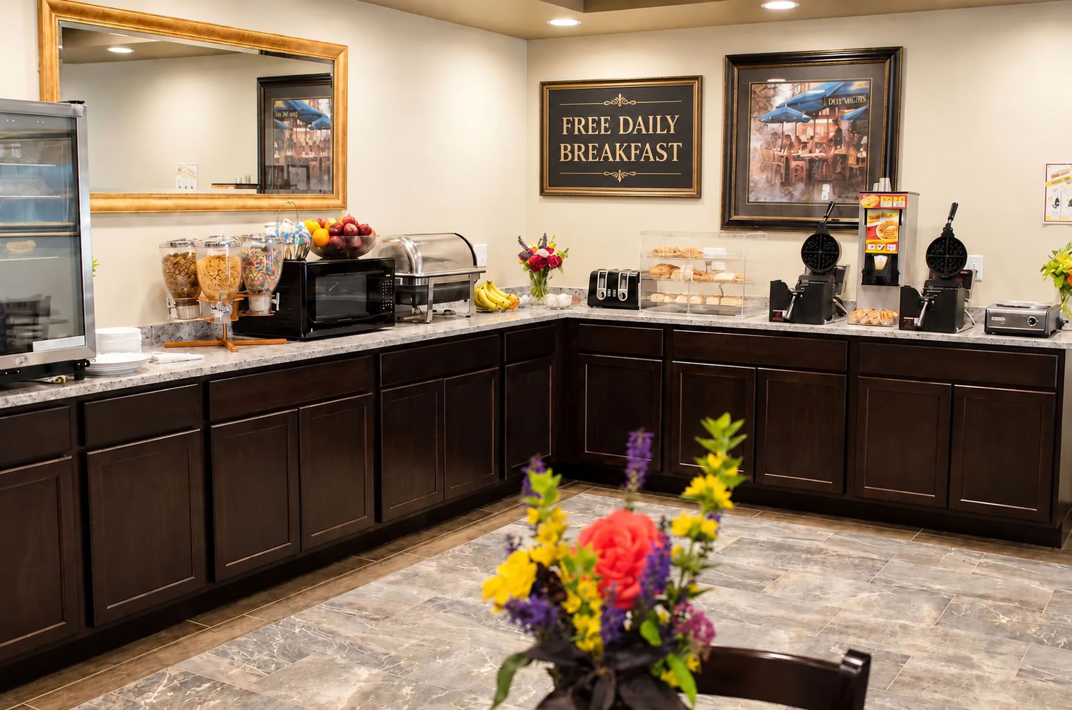 A hotel kitchen with a sign for free daily breakfast, a microwave, and various food items.