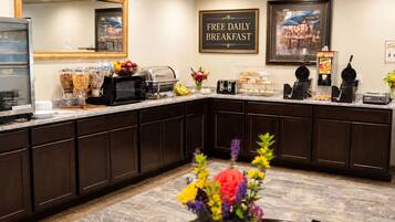 A hotel kitchen with a sign for free daily breakfast, a microwave, and various food items.