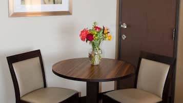 Een hotelkamer met een ronde houten tafel, twee stoelen, een vaas met bloemen, een lijst met een afbeelding aan de muur en een gesloten deur.