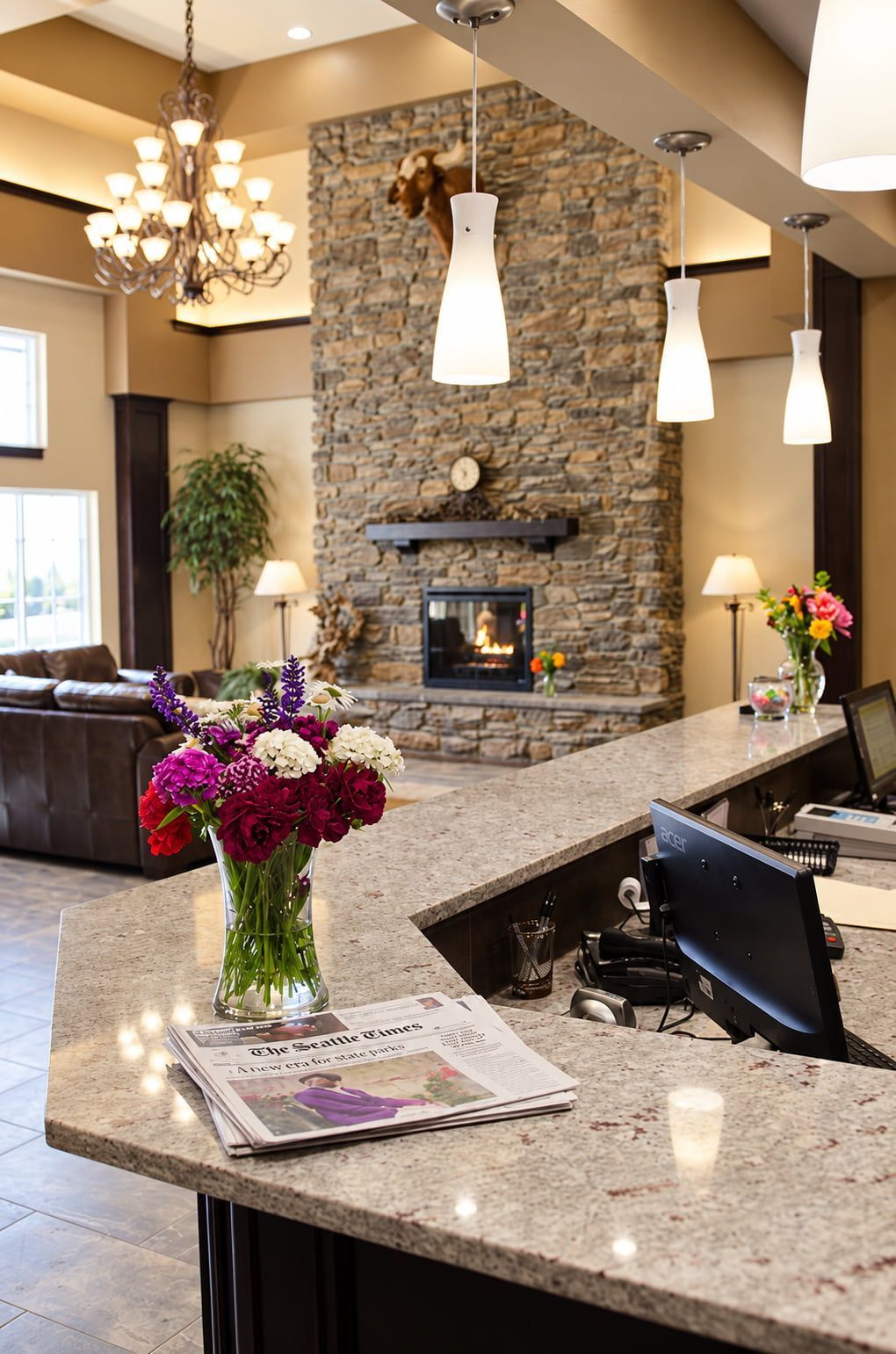 A hotel reception area with a stone fireplace, a vase of flowers, and a newspaper on the counter.