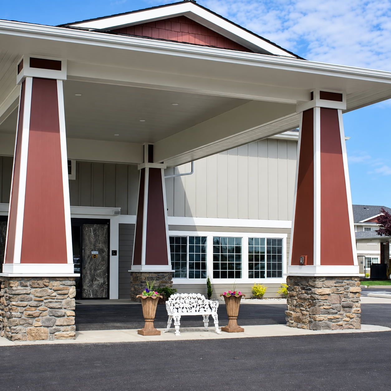 A building with a covered entrance, stone pillars, and a bench with potted plants.