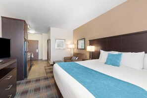 A hotel room with a large bed, a television, a desk, and a chair. - Accessible King Room w/ Kitchen | Free Breakfast! (Moses Lake)