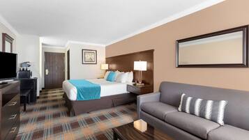 A hotel room with a bed, a sofa, a desk with a television, and a coffee machine.