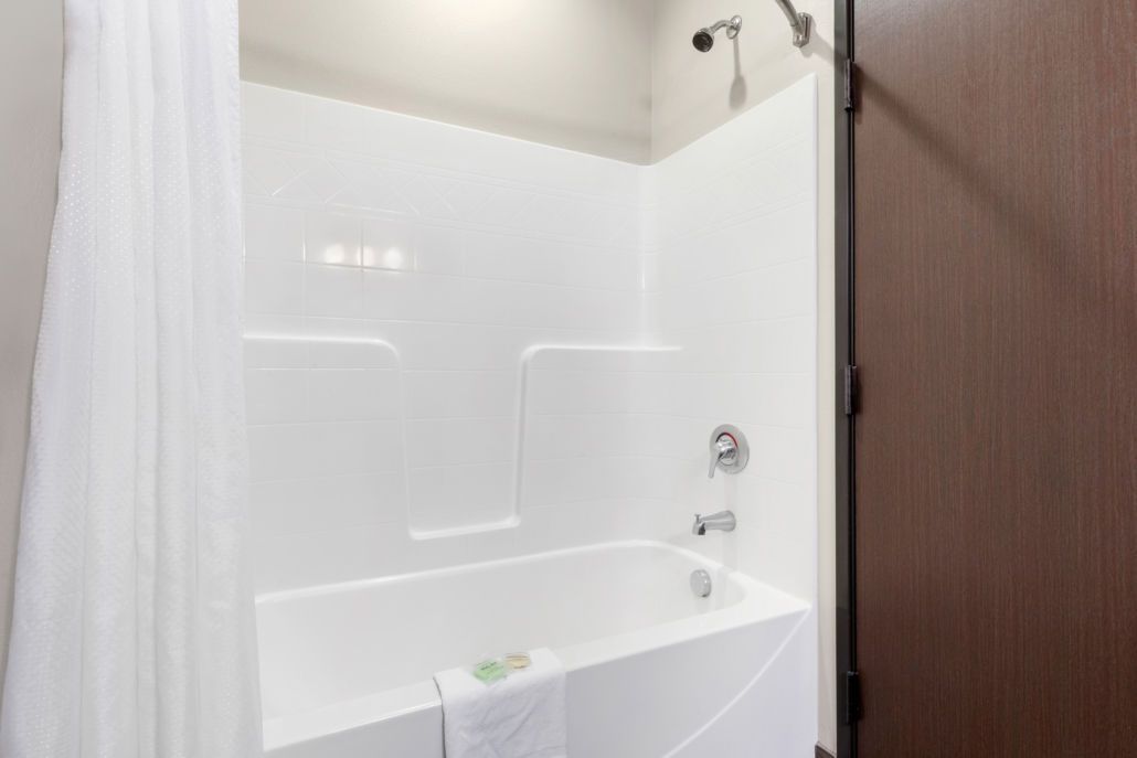 Una vasca da bagno bianca con un soffione, un asciugamano e una porta sulla destra.