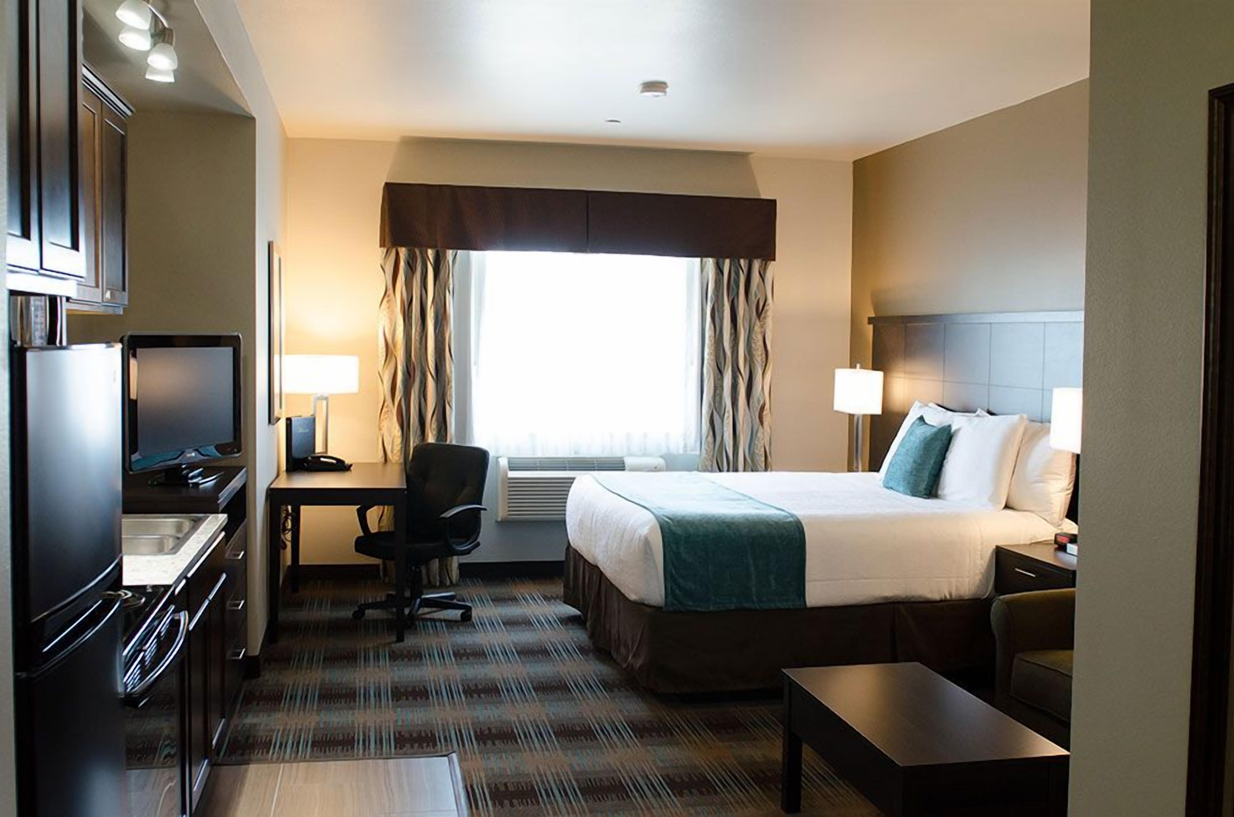 A hotel room with a bed, desk, chair, and kitchenette.