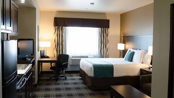 A hotel room with a bed, desk, chair, and kitchenette.