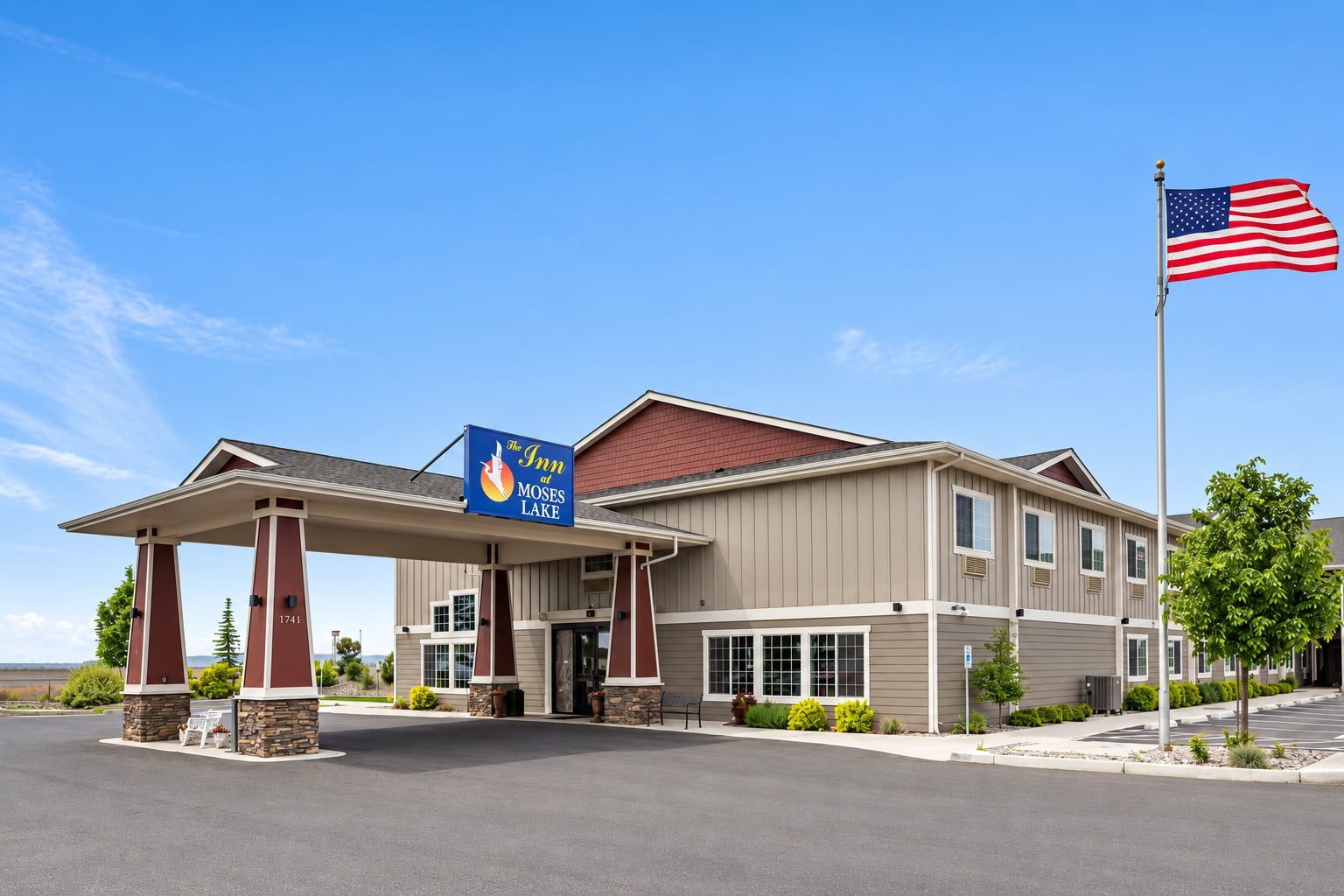A hotel with a covered entrance, a flag, and a sign indicating it's The Inn at Moses Lake.