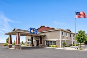 Et hotel med overdækket indgang, et flag og et skilt, der viser, at det er The Inn at Moses Lake.