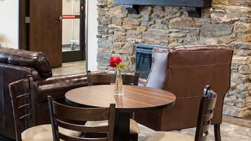 A dining area with a stone wall, a flat-screen TV mounted above a fireplace, leather seating, and a round wooden table.