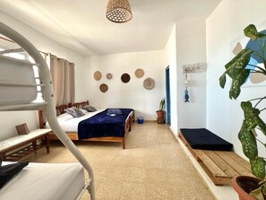 A bedroom with a bunk bed, a single bed, a bedside table, a potted plant, and a wall-mounted shelf. - CASA GRECA (Río Hato)