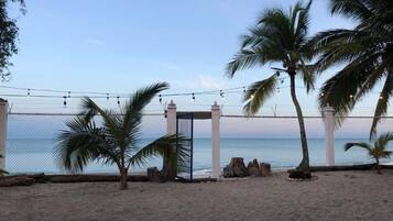A beach with a fence, palm trees, and a view of the ocean.