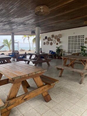 An outdoor seating area with wooden tables and benches, a wall with decorative plates, and a view of the beach. - CASA GRECA (Río Hato)
