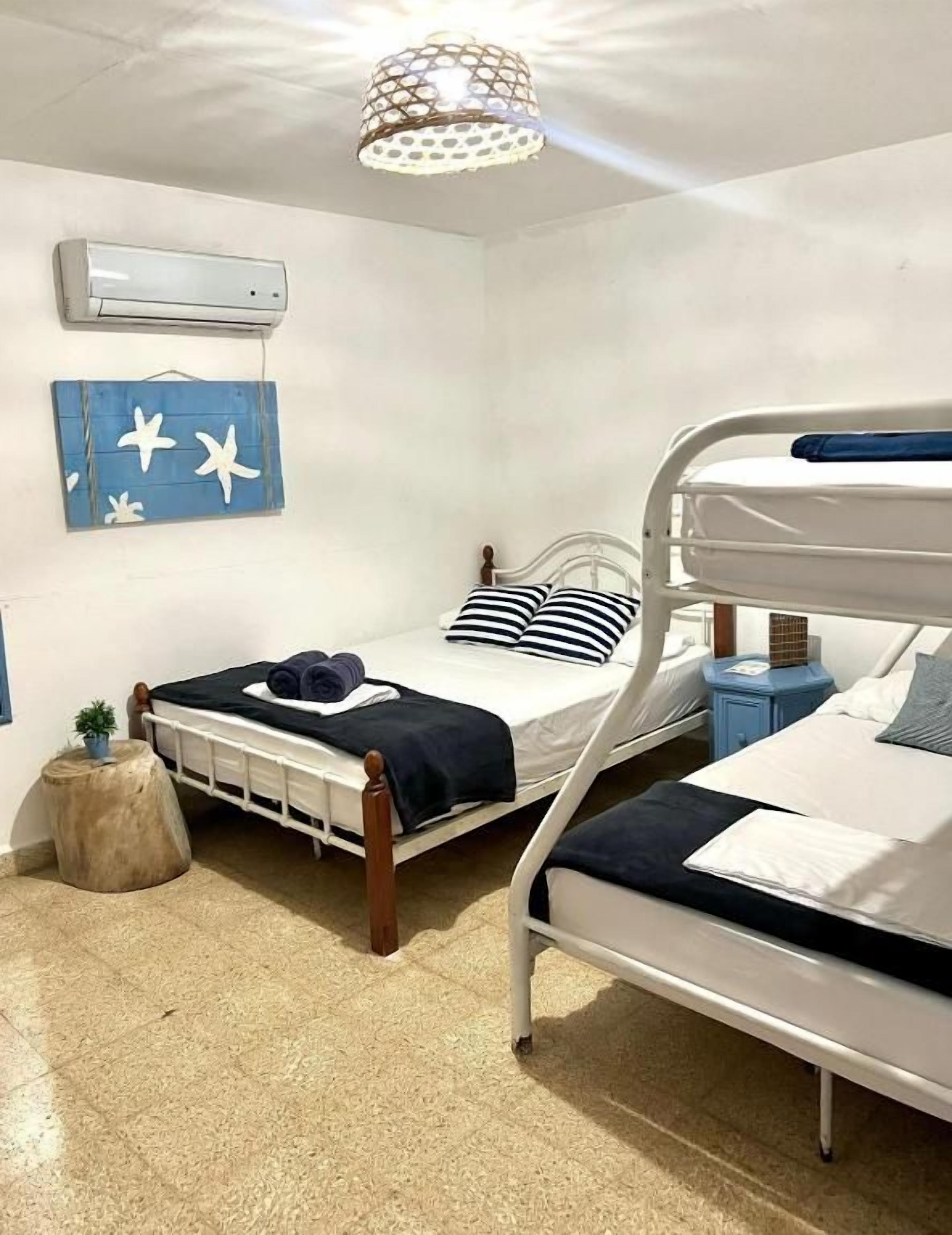 Una habitación con dos literas, una mesita redonda pequeña, aire acondicionado de pared y una lámpara en el techo.