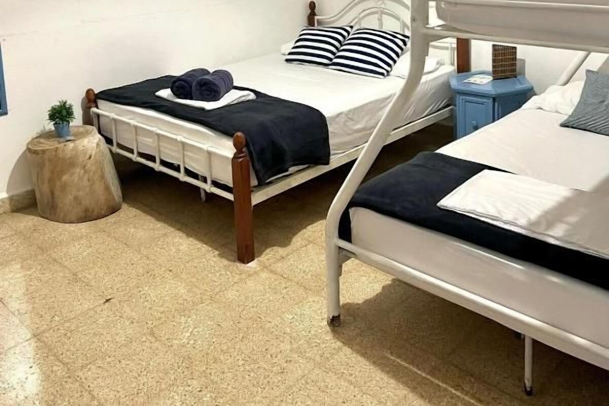A room with two bunk beds, a small round table, a wall-mounted air conditioner, and a ceiling light fixture.