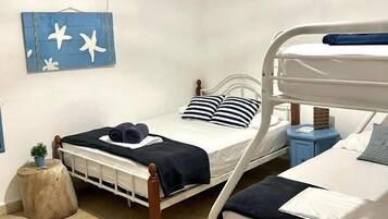 Una habitación con dos literas, una mesita redonda pequeña, aire acondicionado de pared y una lámpara en el techo.