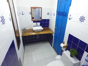 A bathroom with a wooden vanity, a white sink, a blue door, and nautical-themed tiles. - CASA GRECA (Río Hato)