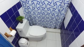 A bathroom with a white toilet, a blue and white patterned shower curtain, and a small potted plant on the toilet tank.