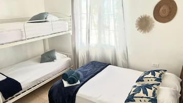 A room with bunk beds, a single bed, a window with sheer curtains, and a wall decoration.