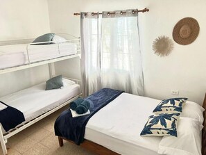 A room with bunk beds, a single bed, a window with sheer curtains, and a wall decoration.