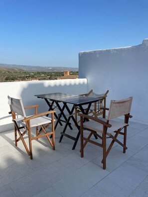 Eine Terrasse mit Tisch und Stühlen, ein freier Blick auf die Landschaft und eine weiße Wand.